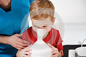 Causian little boy making inhalation with nebulizer at hospital