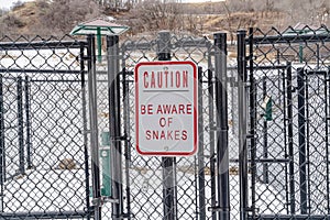 Caution Be Aware of Snakes sign on the chain link fence of a recreational park