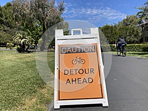Caution. Detour ahead warning sign with bicycle emblem. Bicyclist is passing by photo