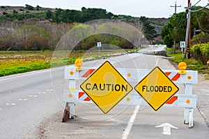 Caution and Flooded warning signs on barricade installed across two-way street to warn drivers about flooded highway