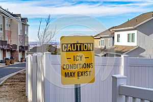 Caution Icy Conditions May Exist yellow sign against houses and white fence