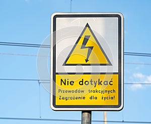 Caution sign with a warning message in Polish against touching overhead electrical wiring indicating a life-threatening hazard