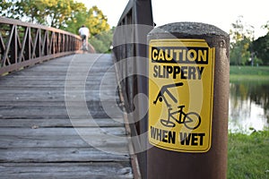 Caution Slippery When Wet Warning Sign with Bike Rider On Bridge