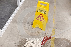 Caution wet floor sign positioned on a concrete surface next to a mop, indicating a freshly cleaned or slippery area