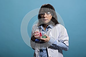 Cautious professional chemistry laboratory worker on blue background having Erlenmeyer glass jars.