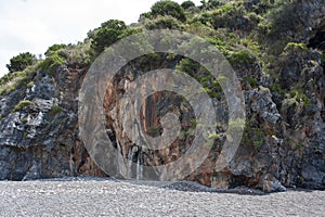 A cave in the cliff running along the beach. Cove, cliffside.