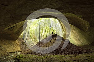 Cave entrance in huge cliff in the forest with man standing in front