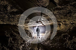 Cave underground with man speleologist and light at entrance