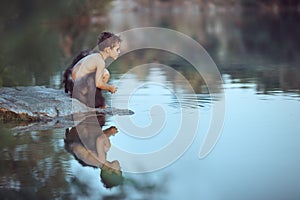 Caveman. Little boy sitting on the beach and looks at the water