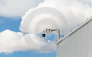 CCD surveillance camera mounted on a hangar in front of a cloudy blue sky
