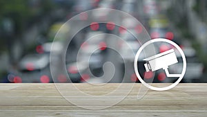 Cctv camera flat icon on wooden table over blur of rush hour with cars and road in city, Business security and safety online conce