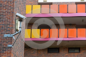 A CCTV camera on the side of council flats showing the colourful balconies in the background, a normal sight on a council estate