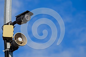 CCTV and loudspeaker alarm on a pole against a blue sky