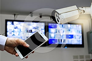 CCTV security camera monitor in office building and a businessman hand holding a smart phone.