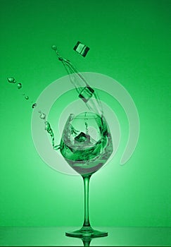 Ce cubes fall into a glass and water is poured out. Water splashing out of a tall wine glass.