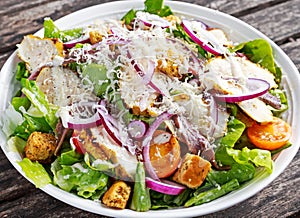 Ceasar salad with grilled chicken fillets, red onion rings, lettuce, orange cherry tomatoes, croutons, grated parmesan