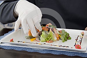 Ceasar salad with shrimps on a plate and hand of kitchener