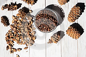 Cedar cones, unshelled pine nuts in glass bowl on white wooden table