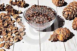 Cedar cones, unshelled pine nuts in glass bowl on white wooden table