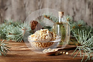 Cedar pine nuts in glass bowl with cones, oil, spoon, cedar brunch on wooden background