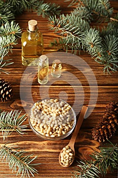 Cedar pine nuts in glass bowl with cones, oil, spoon, cedar brunch on wooden background