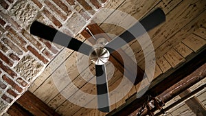 Ceiling air fan slowly spinning on old antique wooden and brick ceiling