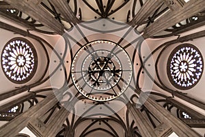 Ceiling of a church with arcades, rose windows and a large hanging candle lamp