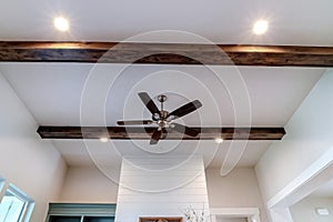 Ceiling fan with lights between decorative wood beams inside living room of home