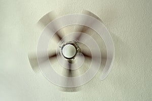 Ceiling fan with spinning blades attached to textured plaster ceiling