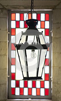 ceiling lamp in iron, in front of the window with glass and stained glass of red squares.