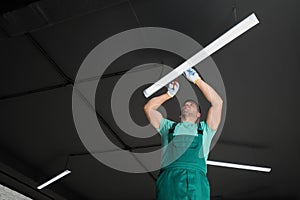 Ceiling light. Electrician installing led linear lamp indoors, low angle view. Space for text