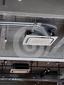 Ceiling mounted cassette type air conditioner decoration near the spot lights on the concrete construction building.