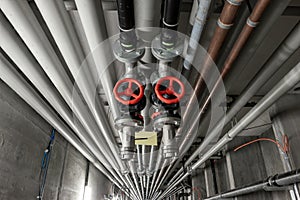 Ceiling mounted industrial pipelines and big round red metal  valve inside underground building, Long corridor with metal floors,