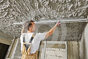 Plasterer smoothing plaster mortar on ceiling with screeder photo