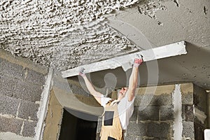 Plasterer smoothing plaster mortar on ceiling with screeder photo