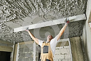 Plasterer smoothing plaster mortar on ceiling with screeder photo