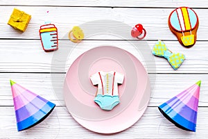 Celebrate child`s birthday. Cookies in shape of baby accesssories, party hats, gift box on white wooden background top