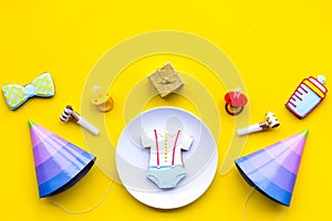 Celebrate child`s birthday. Cookies in shape of baby accesssories, party hats, gift box on yellow background top view