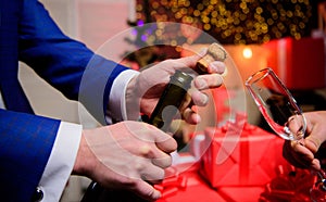 Celebrate new year with champagne. Hands opening champagne bottle and hold glass christmas decorations background