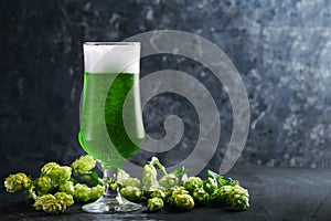 Celebrate St. Patrick`s Day, a glass of Irish green beer on a dark table, green hops and copy space