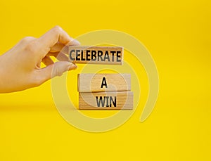 Celebrate a win symbol. Concept words Celebrate a win on wooden blocks. Businessman hand. Beautiful yellow background. Business