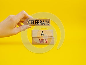 Celebrate a win symbol. Concept words Celebrate a win on wooden blocks. Businessman hand. Beautiful yellow background. Business