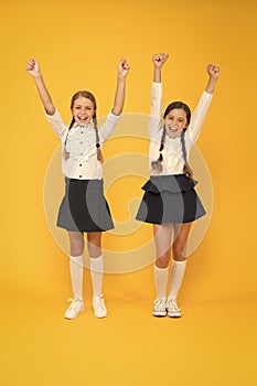 Celebrating back to school. Happy girls celebrating achievement in study on yellow background. Small cute schoolchildren