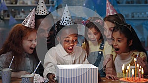 Celebrating birthday party. Afro american little kid opening present box and smiling. Diverse cheerful children, man and