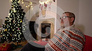 Celebrating Christmas alone. Christmas during lockdown. Mature man sitting by fire place in living room at home. Senior