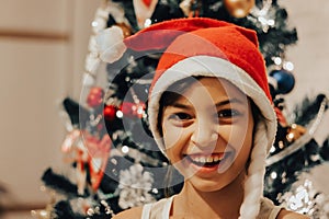 Celebrating Christmas at home lifestyle portrait of laughing teen girl in red Santa hat with Xmas tree on background