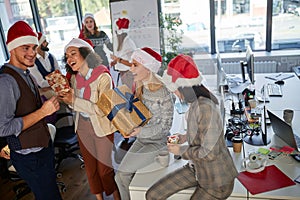 Celebrating Christmas in office.Group of people in santa hat with Christmas present