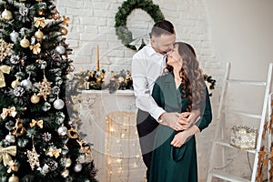 Celebrating Christmas together. Young couple in holiday clothes hugging near the Christmas tree. New Year, Valentine, love,