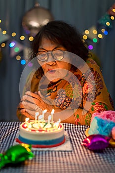 Celebrating elderly woman birthday, blowing candles on homemade baked cake, indoor. Birthday party for seniors woman