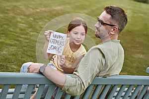 Celebrating Happy Fathers Day outdoors. Young loving father sitting on the wooden bench in park with his cute little